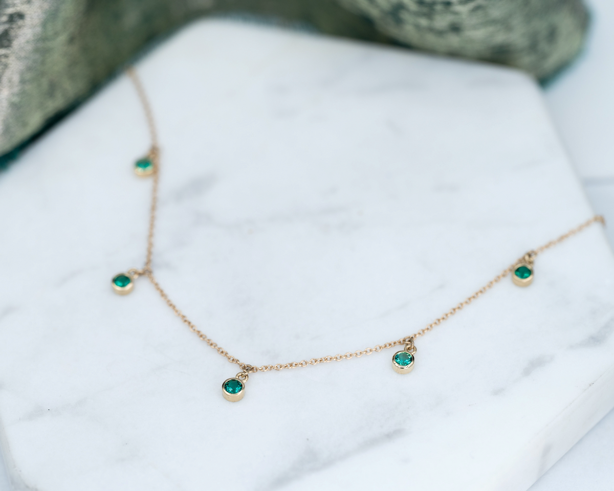 Stórica Studio Harbor Lights necklace featuring five bezel-set green emerald birthstones on a 14k gold cable chain.