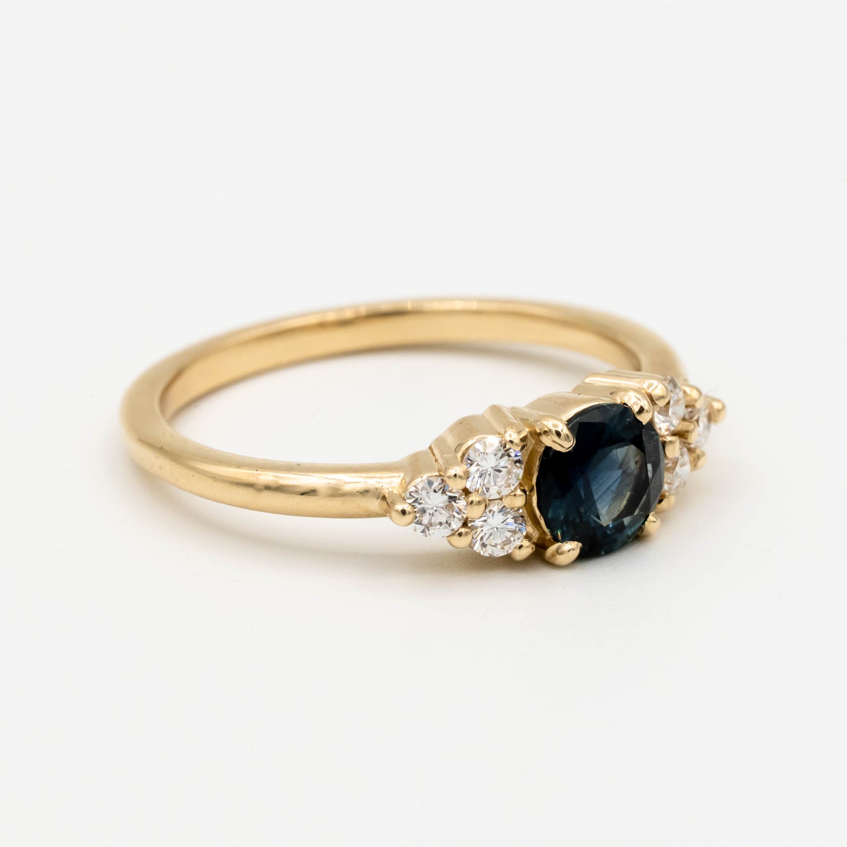 Holly Ring, a core setting style from Storica, featuring a .74ct denim blue Montana sapphire with six 2mm round brilliant lab-grown diamonds, set in a 14k yellow gold band.