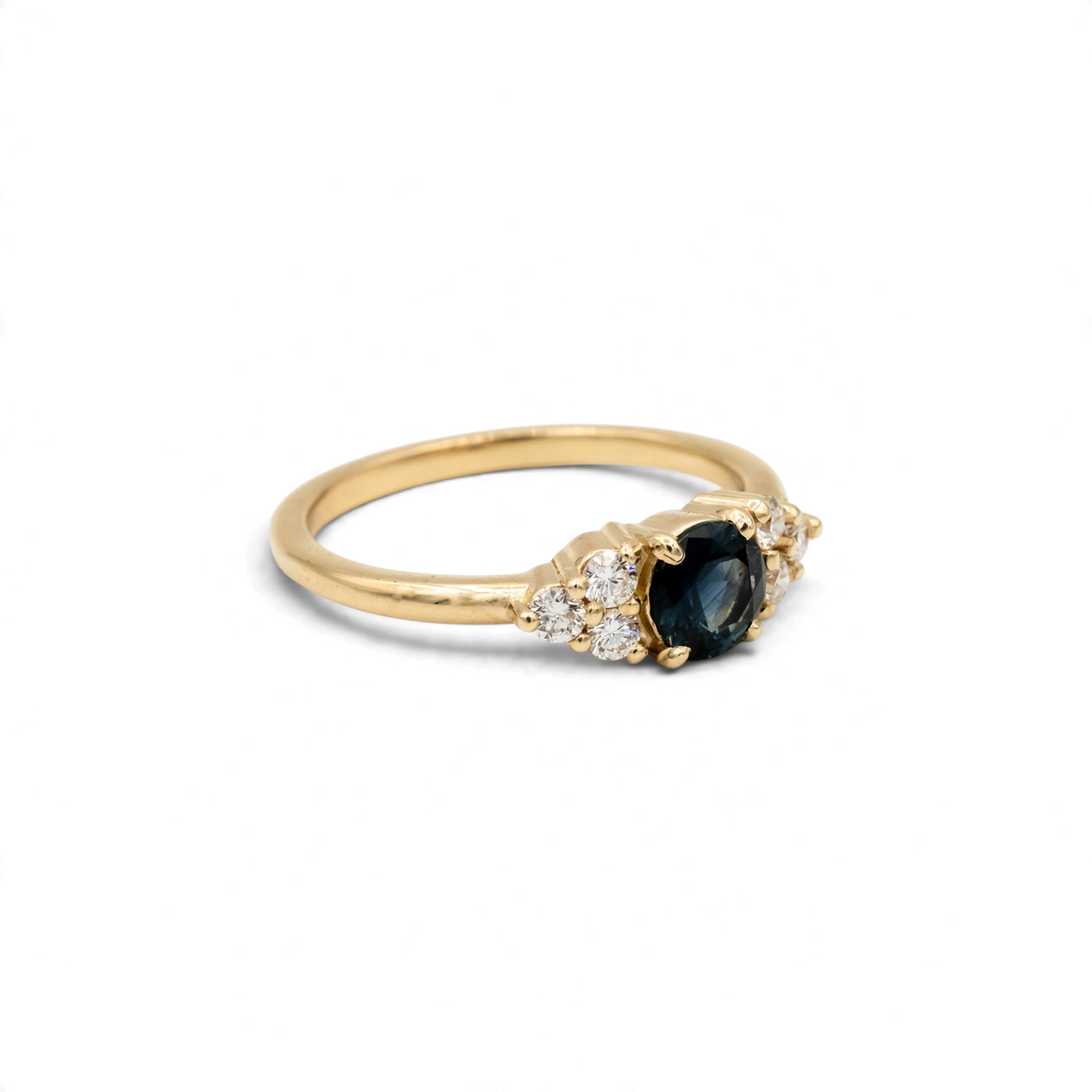 Holly Ring, a core setting style from Storica, featuring a .74ct denim blue Montana sapphire with six 2mm round brilliant lab-grown diamonds, set in a 14k yellow gold band.