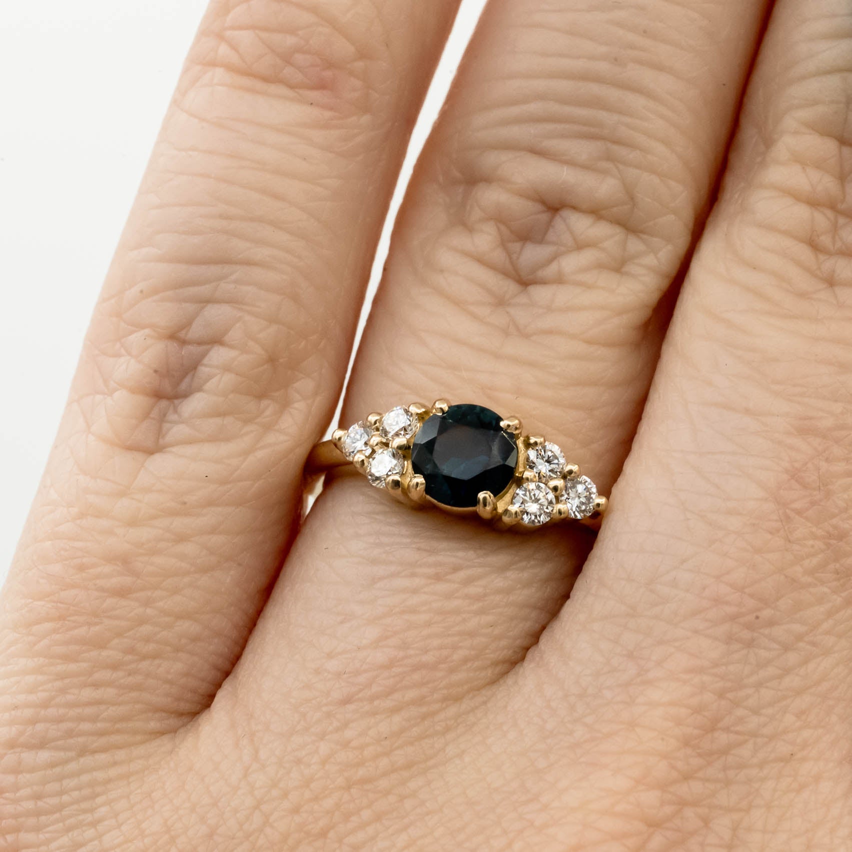 Holly Ring, a core setting style from Storica, featuring a .74ct denim blue Montana sapphire with six 2mm round brilliant lab-grown diamonds, set in a 14k yellow gold band.