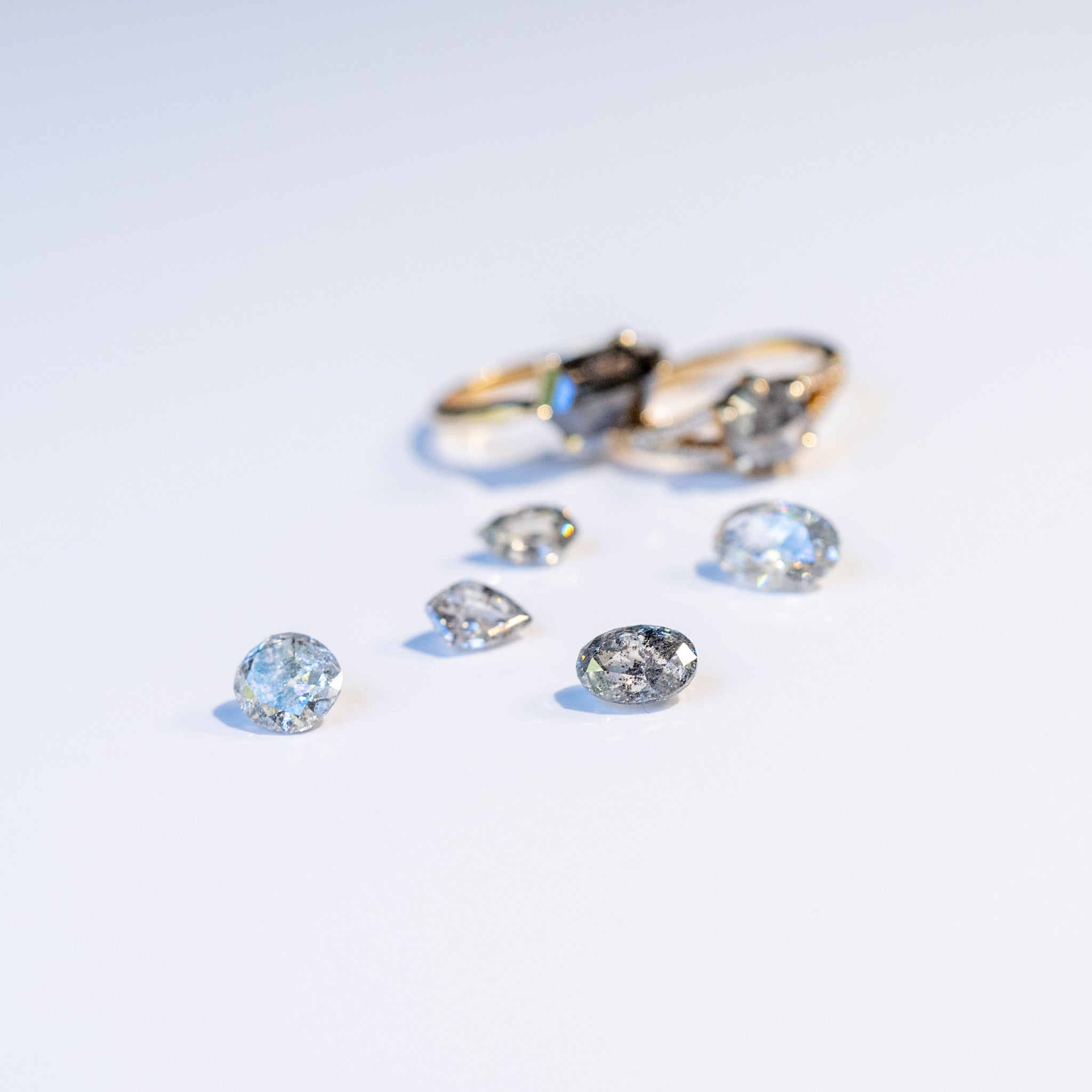 Loose gemstones scattered on a white background with two gold rings in the background.