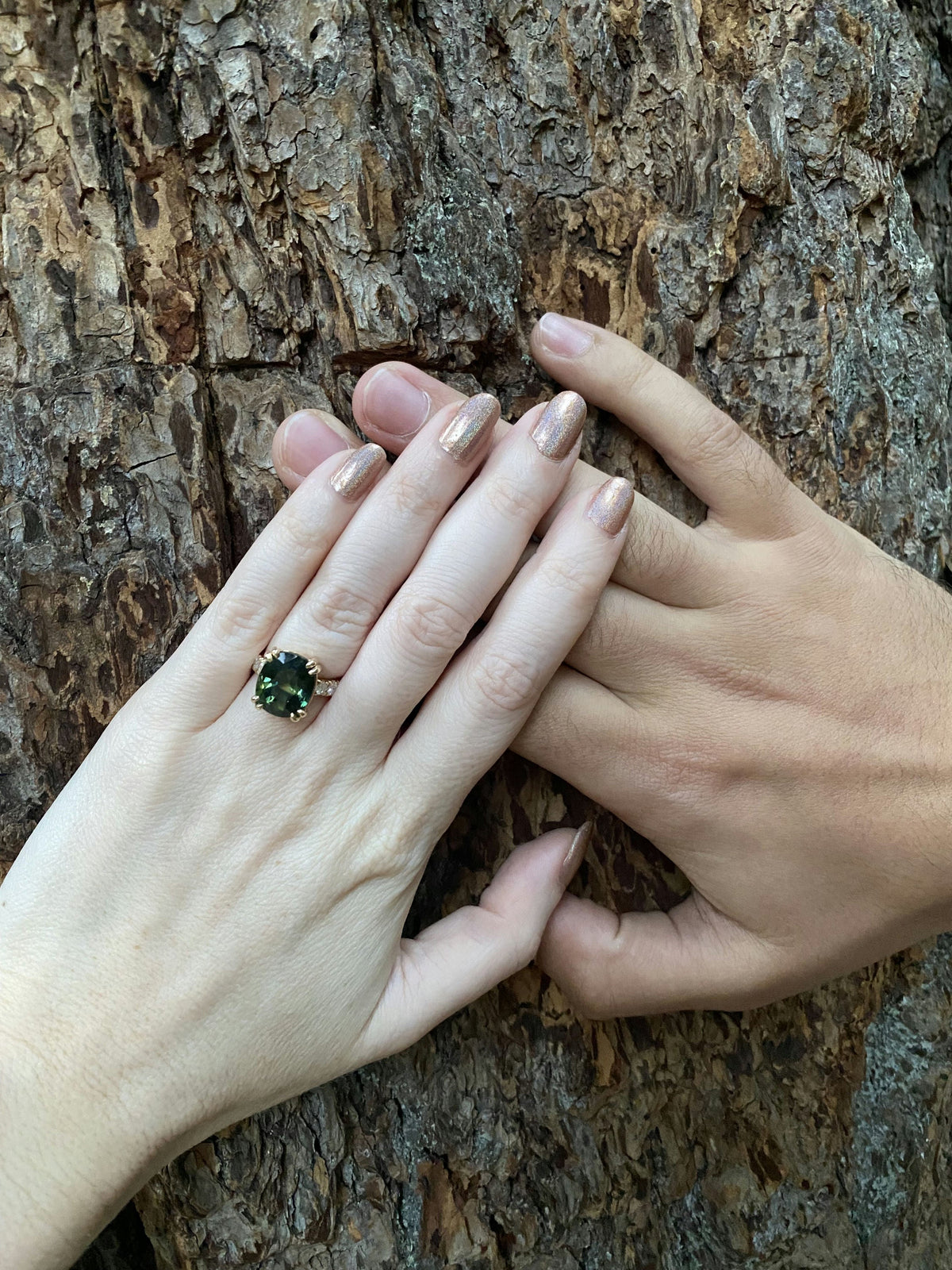 A 7.4 ct green sapphire engagement ring with heirloom pavé diamonds, worn on the hand against tree bark