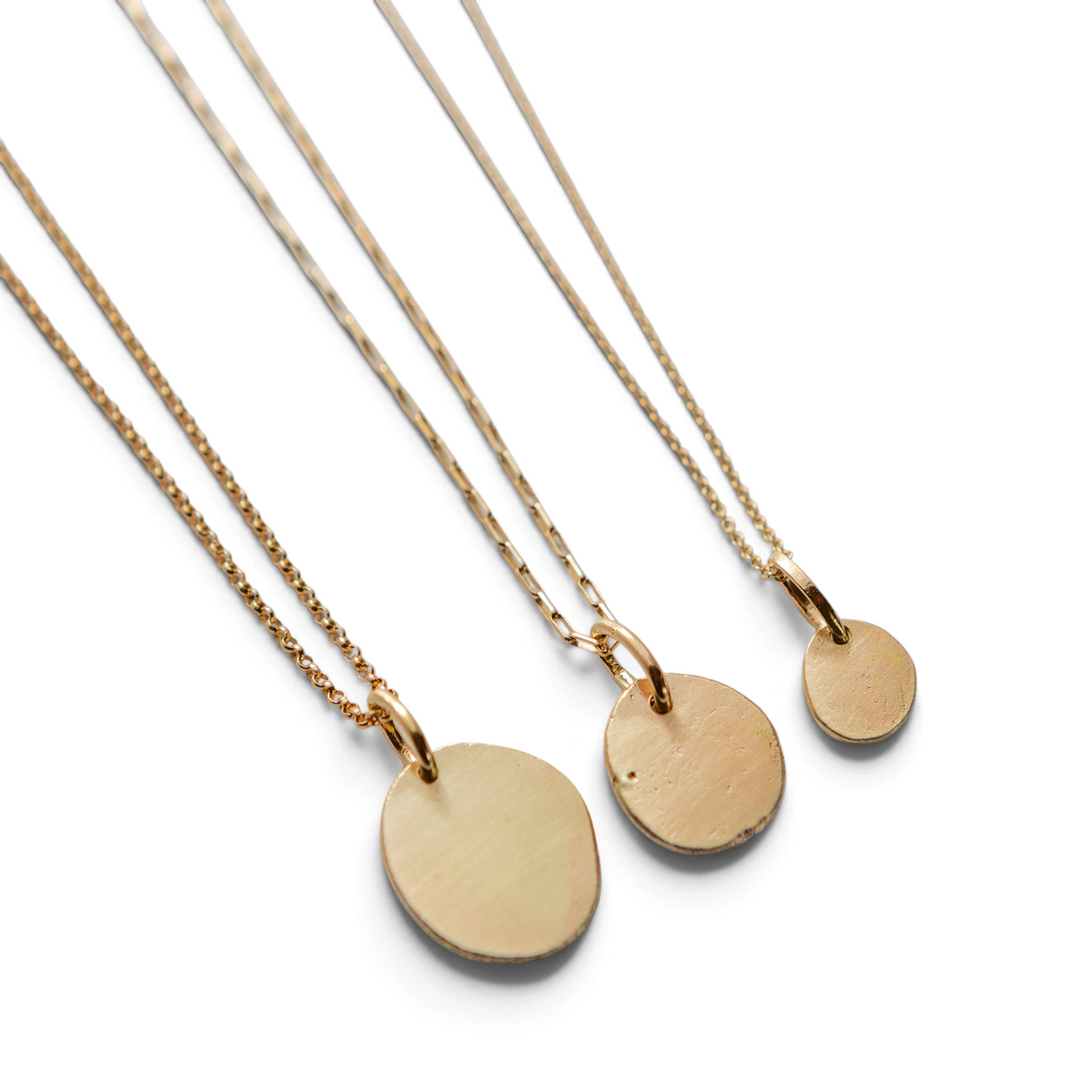 Stórica Studio handmade gold relic charms in three sizes on delicate gold chains against a light textured background.