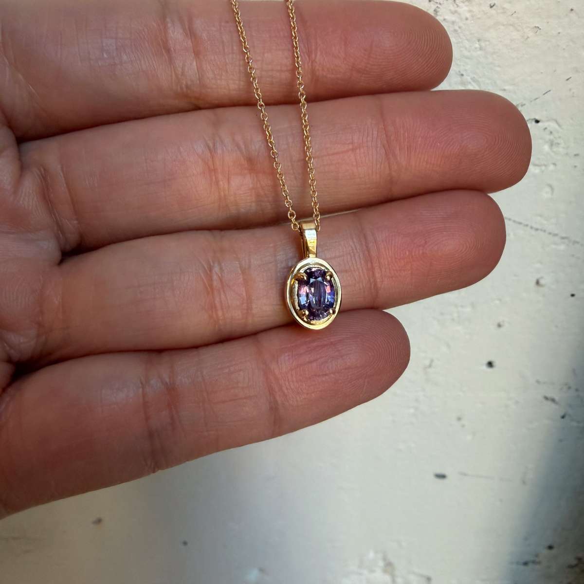 Aster purple sapphire charm held in the palm to show its small size