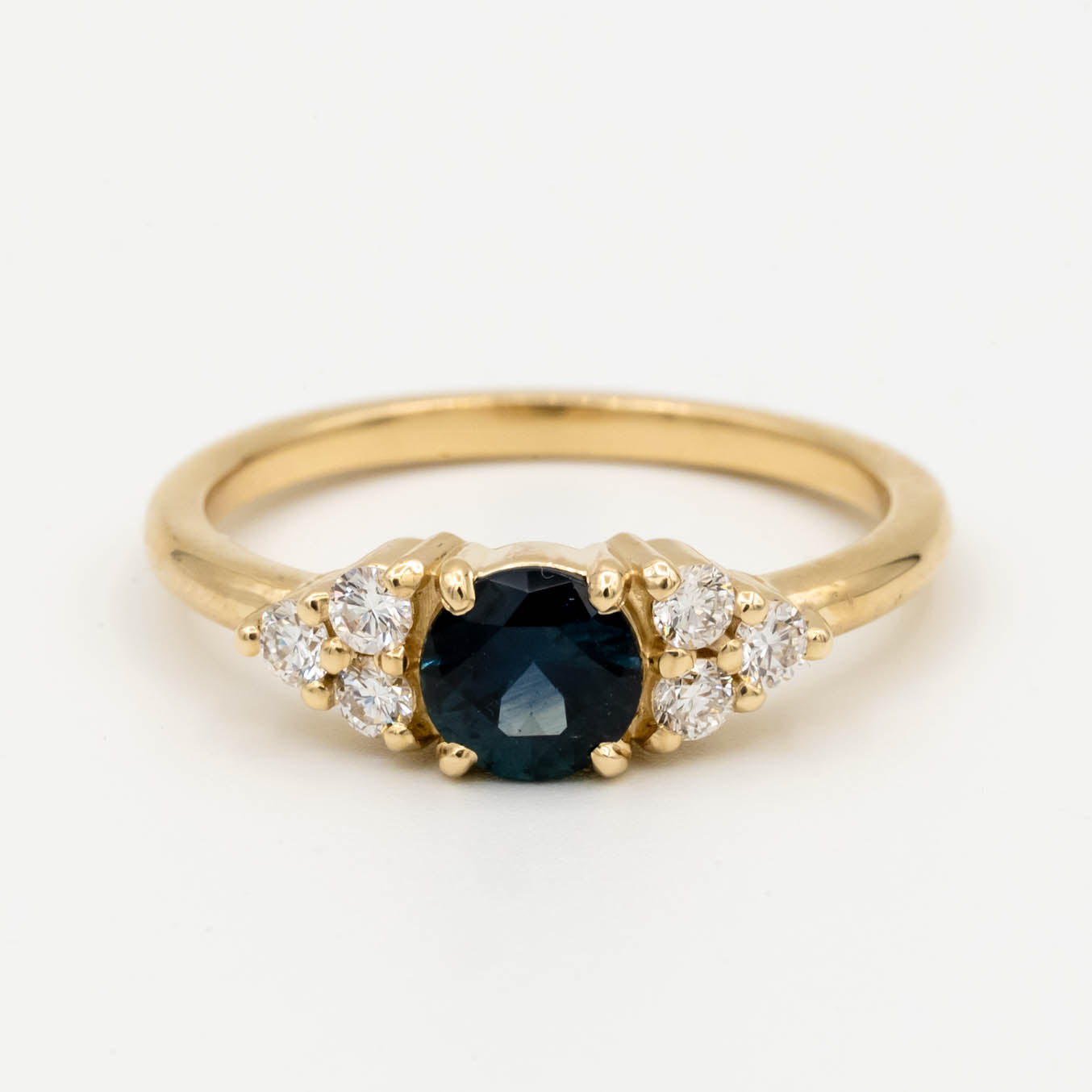 Holly Ring, a core setting style from Storica, featuring a .74ct denim blue Montana sapphire with six 2mm round brilliant lab-grown diamonds, set in a 14k yellow gold band.