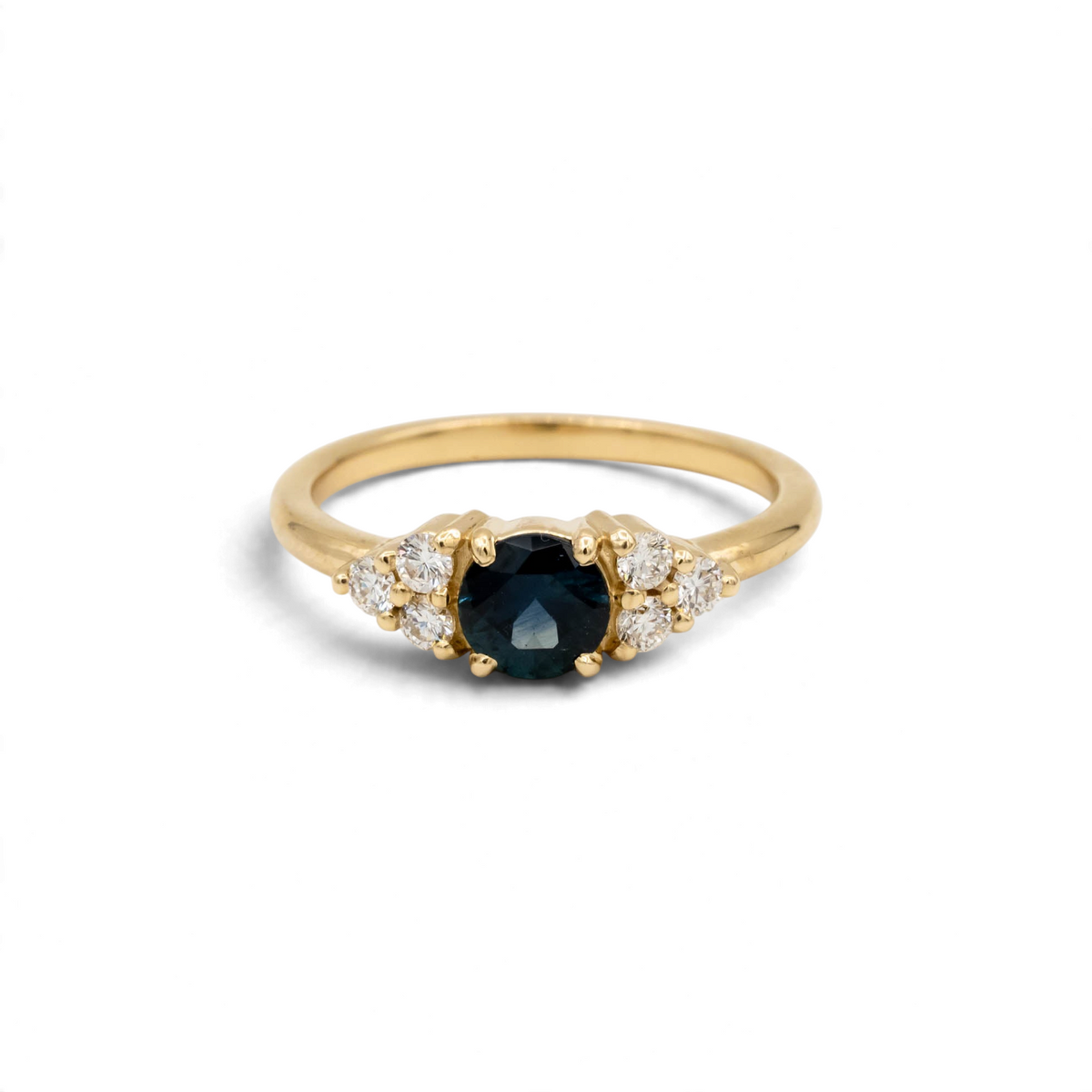 Holly Ring, a core setting style from Storica, featuring a .74ct denim blue Montana sapphire with six 2mm round brilliant lab-grown diamonds, set in a 14k yellow gold band.