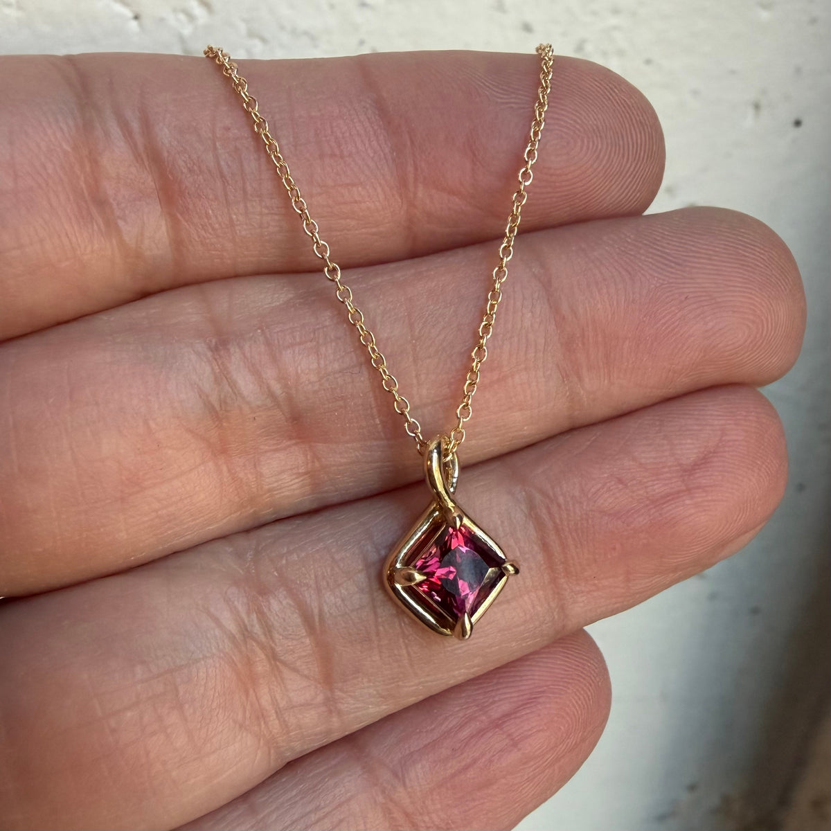 Dahlia raspberry spinel charm on an 18 inch 14k gold cable chain, held in the fingers to show its small size