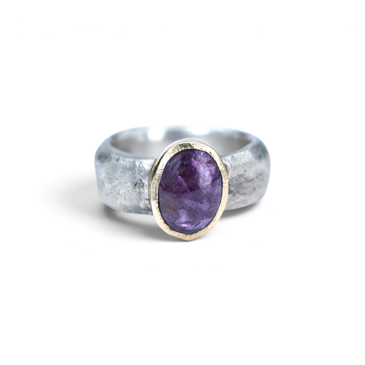 Clio ring with a pinkish-purple sapphire cabochon in a 14k gold bezel on a sandcast sterling silver band