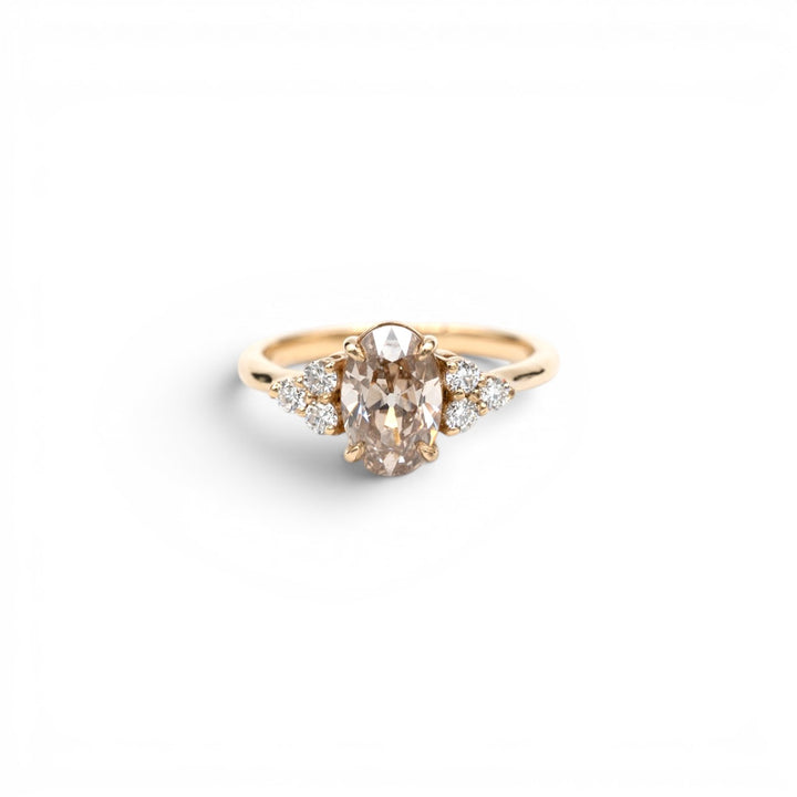 Stórica Studio custom engagement rings Seattle, the Holly ring featuring a 1.63ct lab-grown champagne oval diamond with white lab-grown diamond side stone clusters in 14k yellow gold, photographed on a white background.