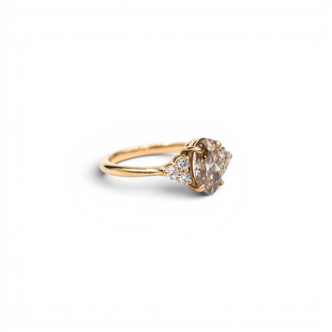 Stórica Studio custom engagement rings Seattle, the Holly ring featuring a 1.63ct lab-grown champagne oval diamond with white lab-grown diamond side stone clusters in 14k yellow gold, photographed on a white background.